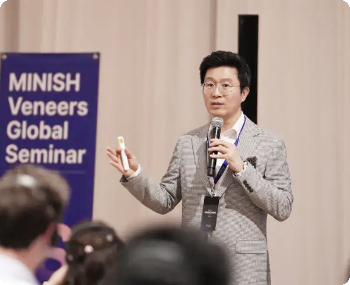 「MINISH Veneers Global Seminar」と書かれた看板の前で、発表者がスライド操作しながら説明する場面